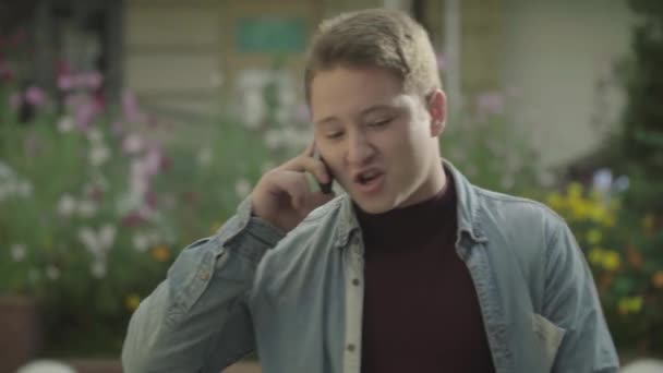 Молодой парень разговаривает по телефону на городской улице — стоковое видео