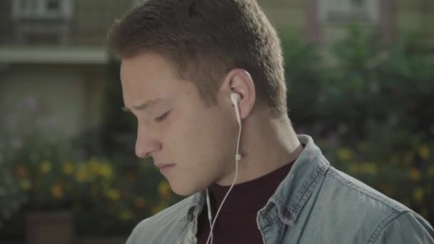 Ein junger Mann mit Kopfhörern kaut an der Keule. Gesicht aus nächster Nähe — Stockvideo