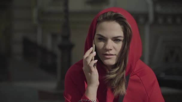 Młoda dziewczyna w czerwoną bluzę mówi przez telefon. — Wideo stockowe