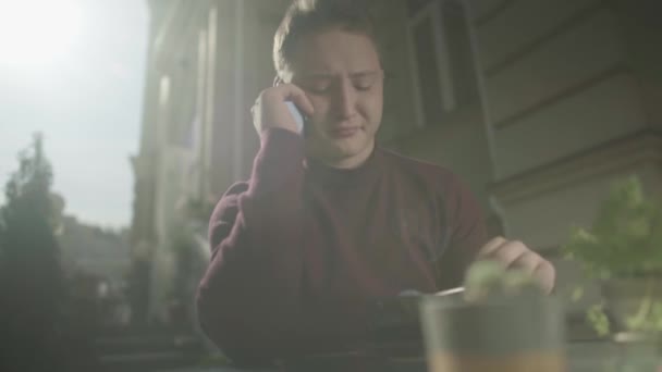 Jovem falando ao telefone em uma mesa em um café — Vídeo de Stock