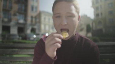 Adam bir bankta otururken zevk ile cips yiyor