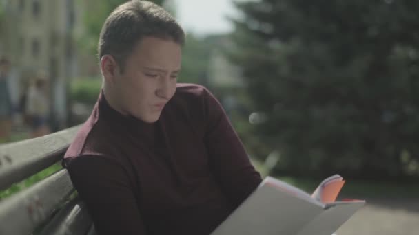 Hombre guapo lee cuidadosamente un libro en el parque — Vídeos de Stock