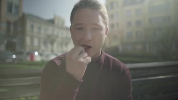 Sonriente chico comiendo patatas fritas en un banco al aire libre — Vídeos de Stock