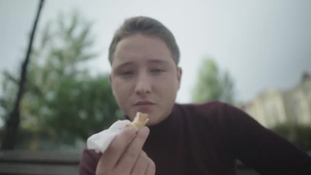 Молодой человек ест бутерброды на улице — стоковое видео
