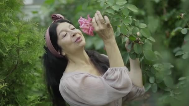 Mujer madura oliendo una rosa en el jardín — Vídeo de stock