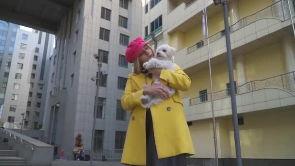 Ξανθιά κυρία κρατάει το σκύλο της στα χέρια της πόλης — Αρχείο Βίντεο