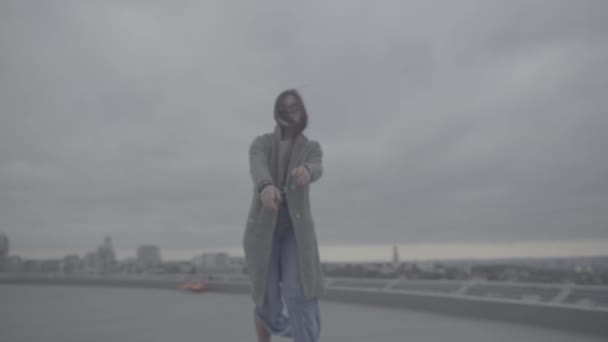 Menina bonita com cabelo escuro em um casaco cinza está de pé ao ar livre — Vídeo de Stock