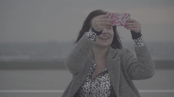 Bella donna con i capelli scuri in un cappotto grigio fa selfie all'aperto. S-log — Video Stock