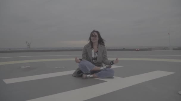 Hermosa chica en abrigo gris sentado en la posición de loto al aire libre. S-log — Vídeo de stock