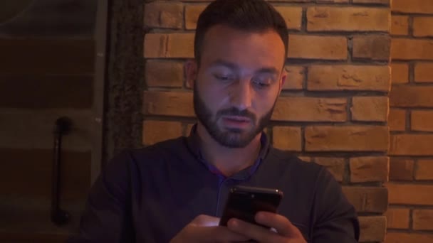 Молодой бородатый парень пишет в телефоне — стоковое видео