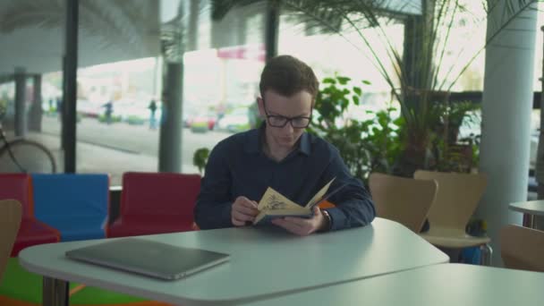 Молодой человек читает книгу в библиотеке — стоковое видео