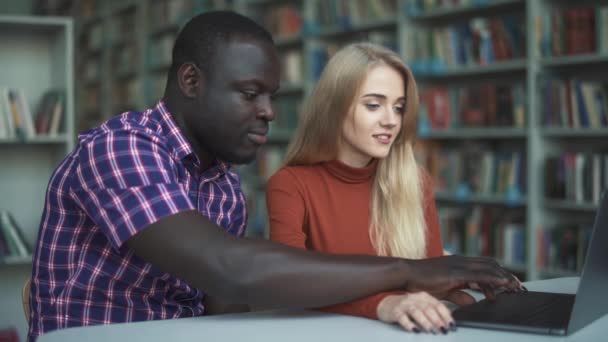 Dama europea y afroamericana pasar tiempo con el ordenador portátil en la biblioteca — Vídeos de Stock