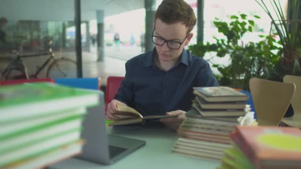 Student studiuje z wielu książek na stole w bibliotece — Wideo stockowe