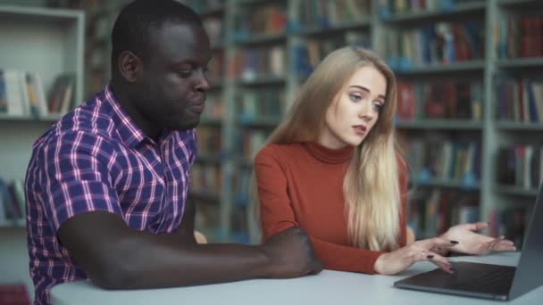 Europäische junge Dame und afrikanisch-amerikanischer Mann lernen in der Bibliothek mit Laptop — Stockvideo