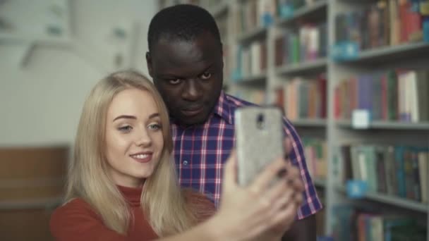 Hombre afroamericano y chica europea se toman selfie en la biblioteca — Vídeos de Stock