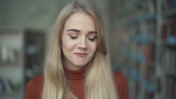 A lány félénken csökkenti a szemét, és mosolyog a kamera — Stock videók