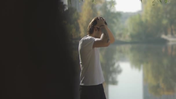 Lång man rätar ut sitt hår tillbaka vid sjön — Stockvideo