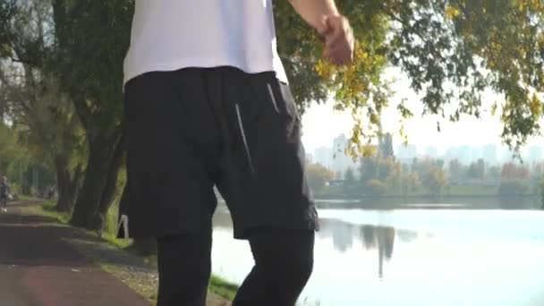 En ung kille körs i den park stannar och dricker vatten ur en flaska — Stockvideo