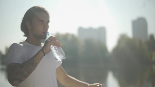 Knappe man drinkt water uit een fles in het park — Stockvideo