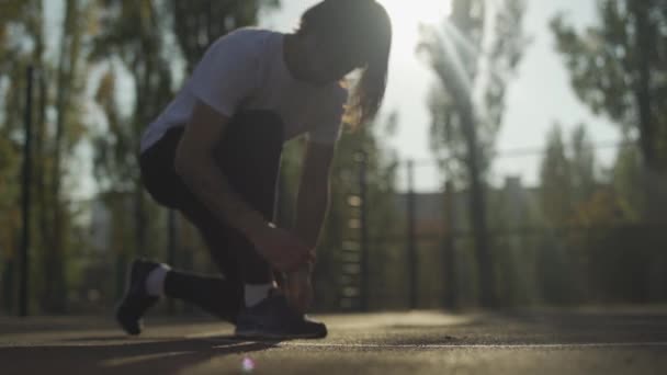 Молодой парень зашнуровывает свои кроссовки снаружи — стоковое видео