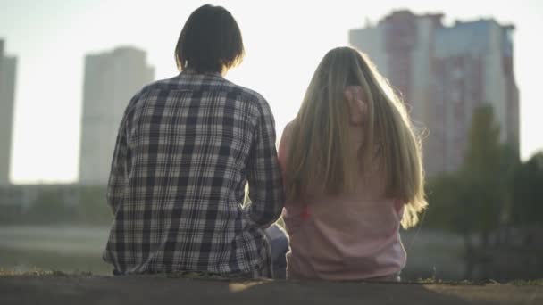 Kille och tjej sitta på flodstranden och titta på staden — Stockvideo