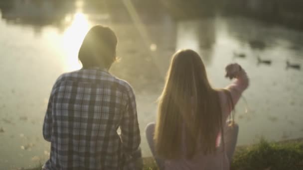 Chico y chica están sentados en la orilla del río — Vídeo de stock