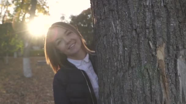 Vacker flicka ser ut bakom ett träd och leenden — Stockvideo