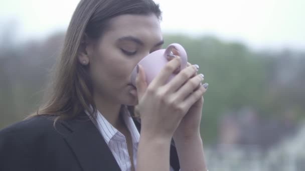 예쁜 여자 음료 뜨거운 커피 야외에서 그녀의 손에 컵 컵 여자의 초상화에서에서 마시는 여자 — 비디오