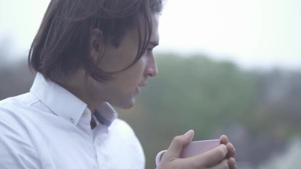 Крупним планом красивий молодий чоловік п'є чашку на відкритому повітрі Портрет чоловіка з чашкою в руках — стокове відео