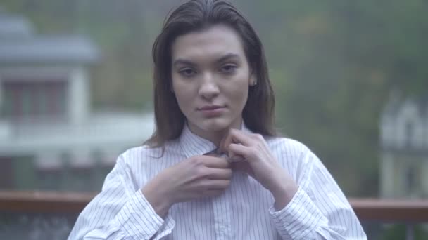 Portret van een jong meisje met lang zwart haar emoties op het gezicht van een mooi meisje mooi meisje zich uitstrekt van de knop op het shirt Brunette in wit overhemd — Stockvideo
