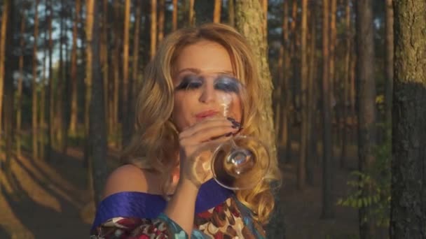 Portrait de femme buvant du vin dans la forêt Dame aux faux cils repose à l'extérieur Fille en robe d'été avec des boissons d'épaule nues vin à l'extérieur Blonde aux yeux verts et aux cils longs — Video