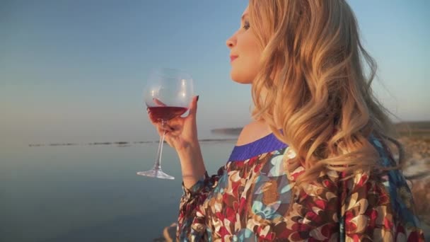 รูปภาพของผู้หญิงผมบลอนด์ ดื่มไวน์ที่ฝั่งทะเล ใกล้ๆ ผู้หญิงหันไปมองกล้อง — วีดีโอสต็อก