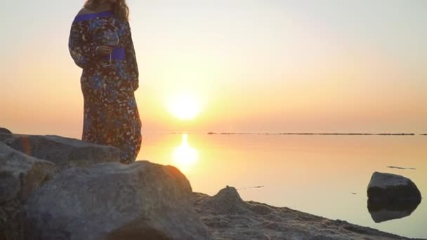 Vrouw in een zomerjurk met een blote schouder wandelingen langs de oever van het meer Cute vrouw wandelingen buiten meisje in zomerjurk met blote schouder dranken wijn buitenshuis — Stockvideo