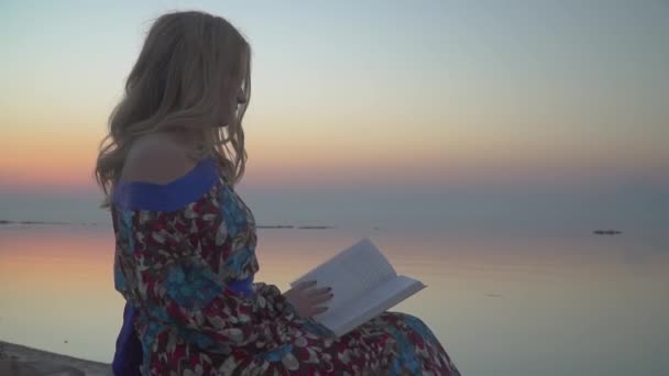 Retrato de mulher loira lendo o livro Feminino está descansando junto ao mar Menina em vestido de verão com ombro nu — Vídeo de Stock