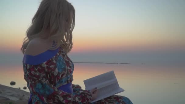 Wanita lucu membaca buku Perempuan beristirahat oleh laut Girl dalam gaun musim panas dengan bahu telanjang — Stok Video