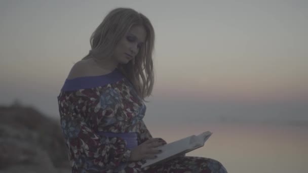 Mujer encantadora leyendo el libro Mujer está descansando junto al mar Chica en vestido de verano con hombro desnudo al aire libre. S-log, sin clasificar — Vídeos de Stock