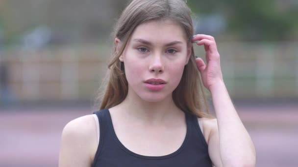 Retrato de uma menina bonito endireita seu cabelo ao ar livre Jovem com belos olhos e lábios suaves endireita suavemente o cabelo e olha para a câmera Uma jovem flerta com a câmera — Vídeo de Stock