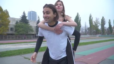 Spor giyim spor giyim yakışıklı adam açık havada güzel genç çift bir kız aşık bir spor stadyumunda futbol topu ile onun geri atletik çift üzerinde tutuyor