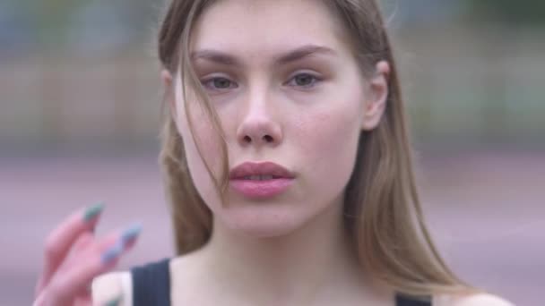 Portrait of a beautiful young girl straightens her hair outdoors Young girl with beautiful eyes and tender lips flirts with the camera — Stock Video