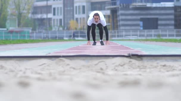 Jeune homme en tenue de sport accélère et saute dans le sable devant la caméra Le sable se disperse sous les pieds d'un sauteur qui a sauté devant la caméra Mode de vie sain — Video