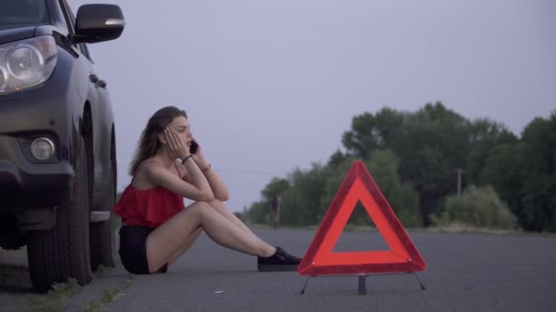 Mujer joven está sentada cerca de coche roto Mujer es triste Mujer está llamando por teléfono móvil Problemas de coche — Vídeos de Stock