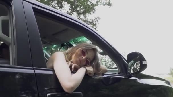 Young girl leans her head out of the car window driving along the road Young couple travels by car Lady in sunglasses Man is driving vehicle — Stock Video