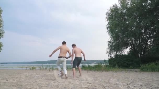 Dos chicos jóvenes jugando al fútbol en el río Competencia entre personas Joven es puntuaciones Amigos divertirse juntos Pasar tiempo al aire libre Estilo de vida activo — Vídeos de Stock