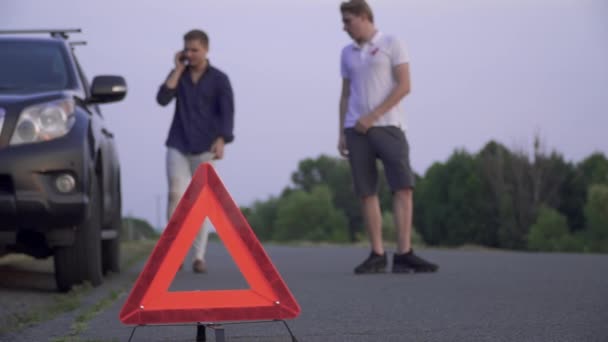 Dos tipos al lado de un coche roto de pie al lado de la carretera. Un tipo pide ayuda por teléfono y el segundo está viendo la rueda Problemas con el coche Concéntrate en el primer plano — Vídeos de Stock