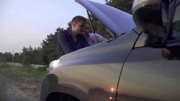 Dos chicos jóvenes miran en el capó abierto de su coche Amigos tienen vehículo roto en el camino Problemas de coche — Vídeo de stock