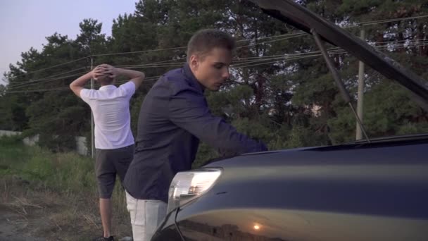 Dois amigos olham para o capô aberto de seu carro Rapazes têm veículo quebrado na estrada Problemas de carro — Vídeo de Stock