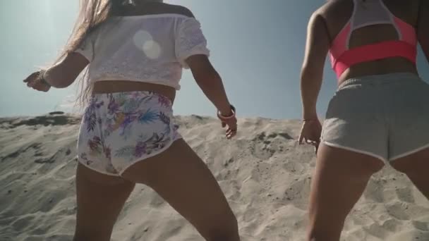 Två heta flickvänner med fina kroppar dansar twerk i korta shorts på stranden söta damer flytta sina rumpor klädd i ljusa shorts kvinnor tillbringa tid utomhus — Stockvideo