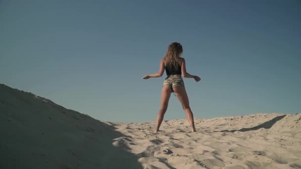 Süßes athletisches Mädchen tanzt Twerk am Strand gebräuntes Mädchen in kurzen Shorts bewegt ihren Körper stehend auf dem Sand — Stockvideo