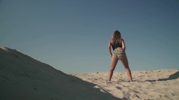 Молодая милая девушка танцует тверк на пляже Загорелая женщина двигает задницей стоя на песке Сексуальная женщина с привлекательным телом трясет задницей Красивая леди танцует страстно — стоковое видео