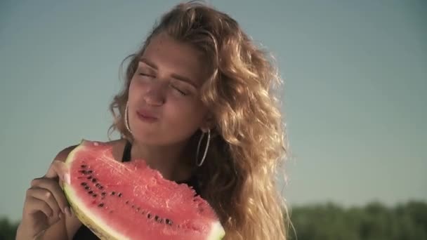 Porträt einer Frau mit wehendem Haar, die Wassermelone im Freien isst Mädchen genießt ihre Ruhe und lächelt — Stockvideo